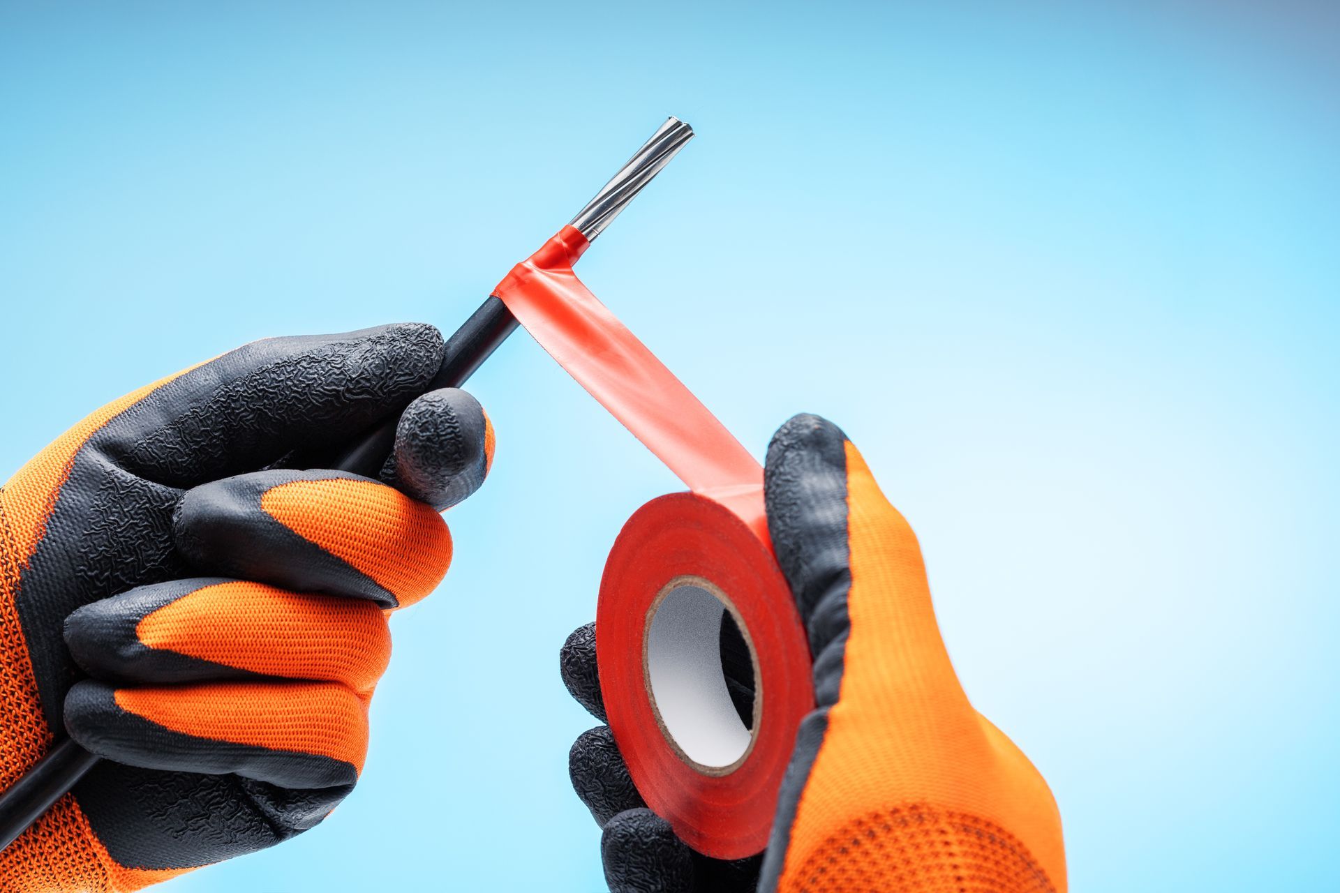 Hands in orange work gloves holding a utility knife and red tape on a blue background. Hands in orange work gloves holding a utility knife and red tape on a blue background.