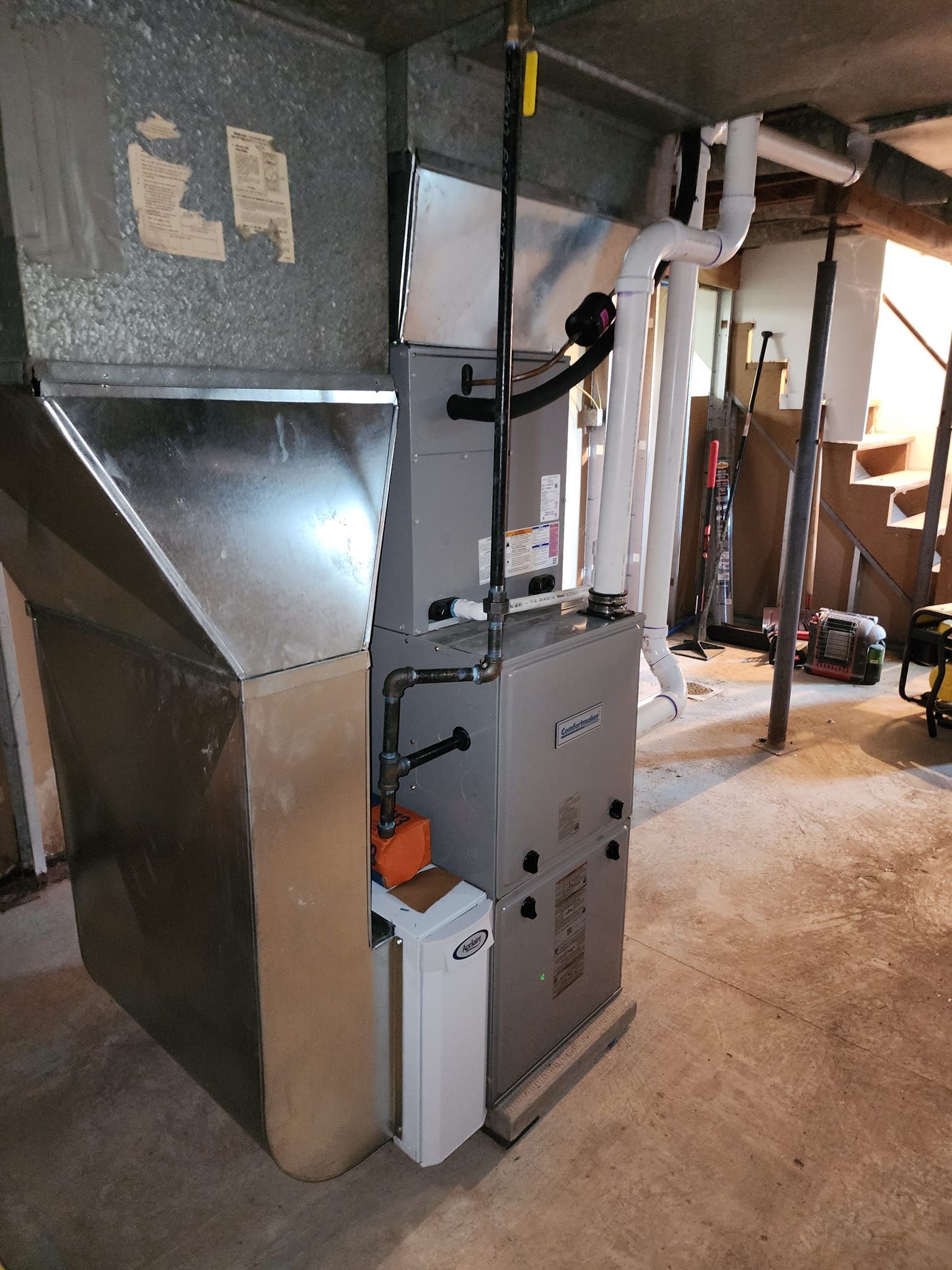 Kenders Heating And Air Conditioning | a furnace is sitting in a basement next to a trash can.