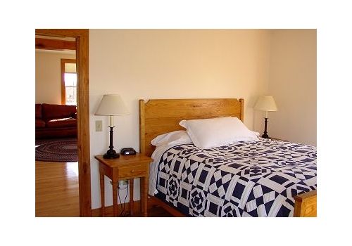 Bedroom with a wooden bed, patterned quilt, bedside lamps, and an open doorway to another room