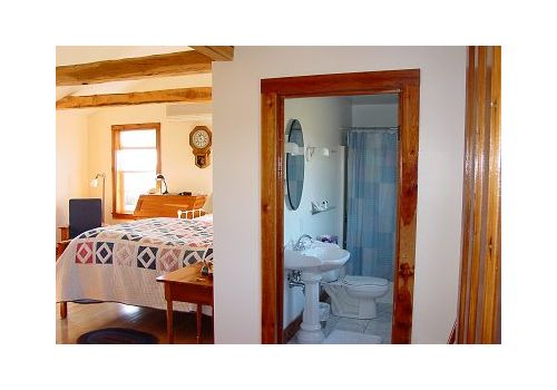 Bedroom with a doorway showing an attached bathroom, wood trim, and a bed with a patterned quilt.