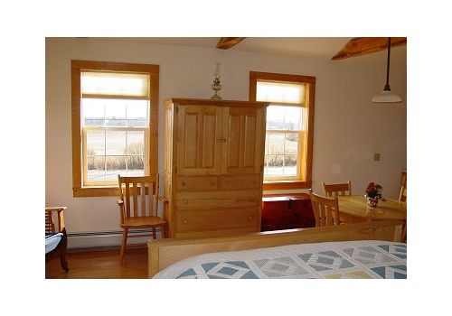 Wooden armoire between two windows in a sunlit bedroom with a bed and chair