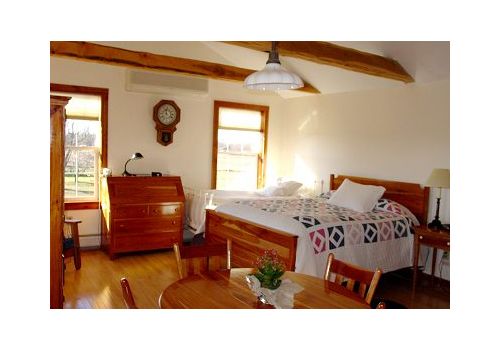 Bright bedroom with wooden beams, bed, dresser, and sunlight through windows