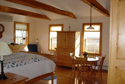 Bedroom with bed, wooden furniture, and dining table near windows with sunlight.