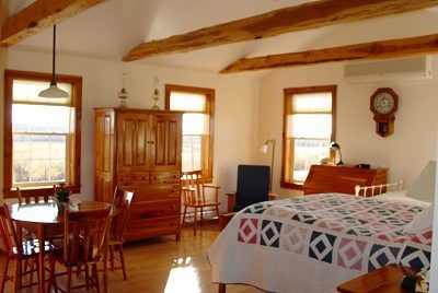 Cozy room with wooden furniture, including a bed, table, and dresser. Windows show a field.