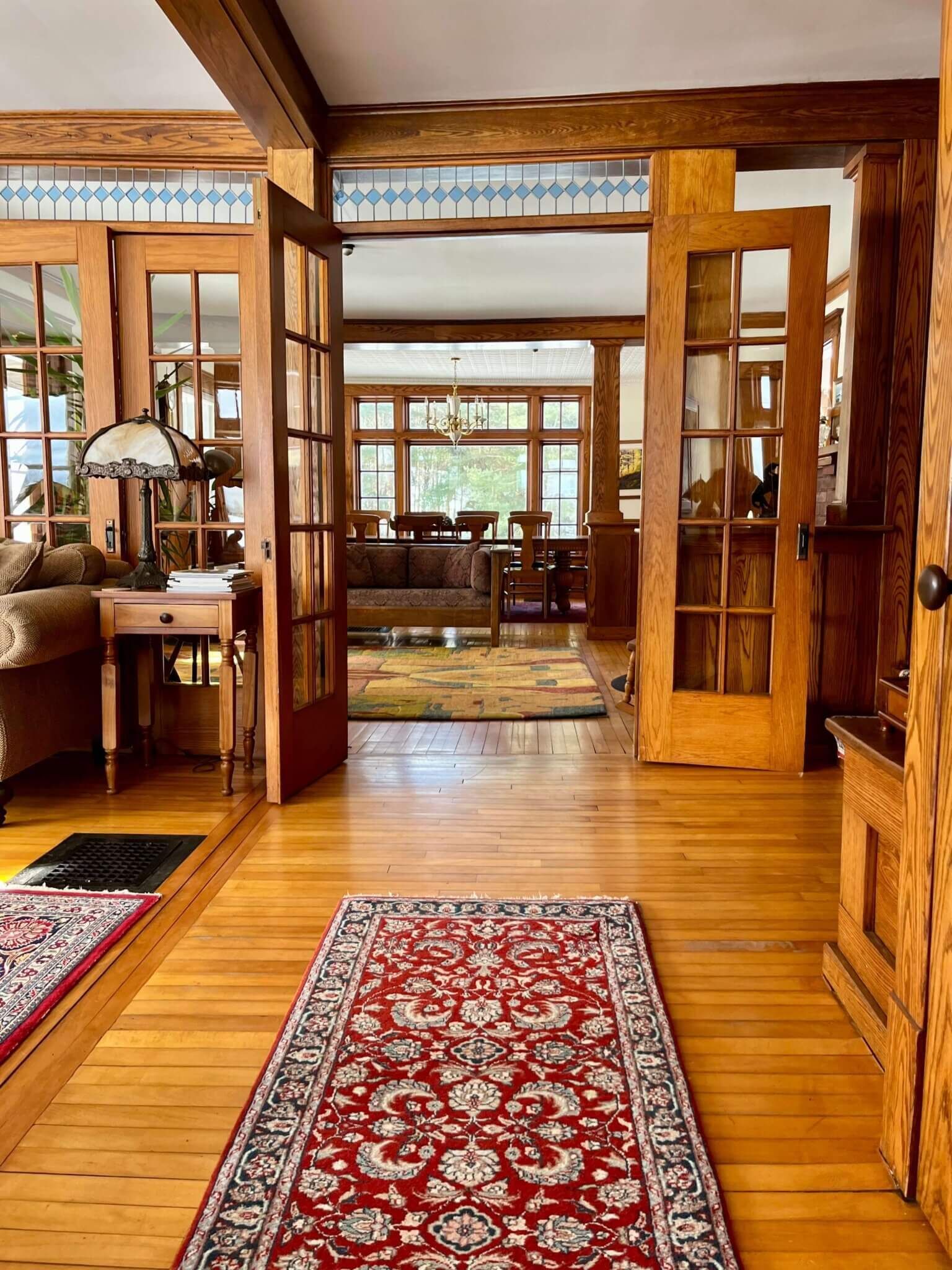 Hardwood hallway with red patterned rug leading to a dining room. Wooden doors, windows, and beams.