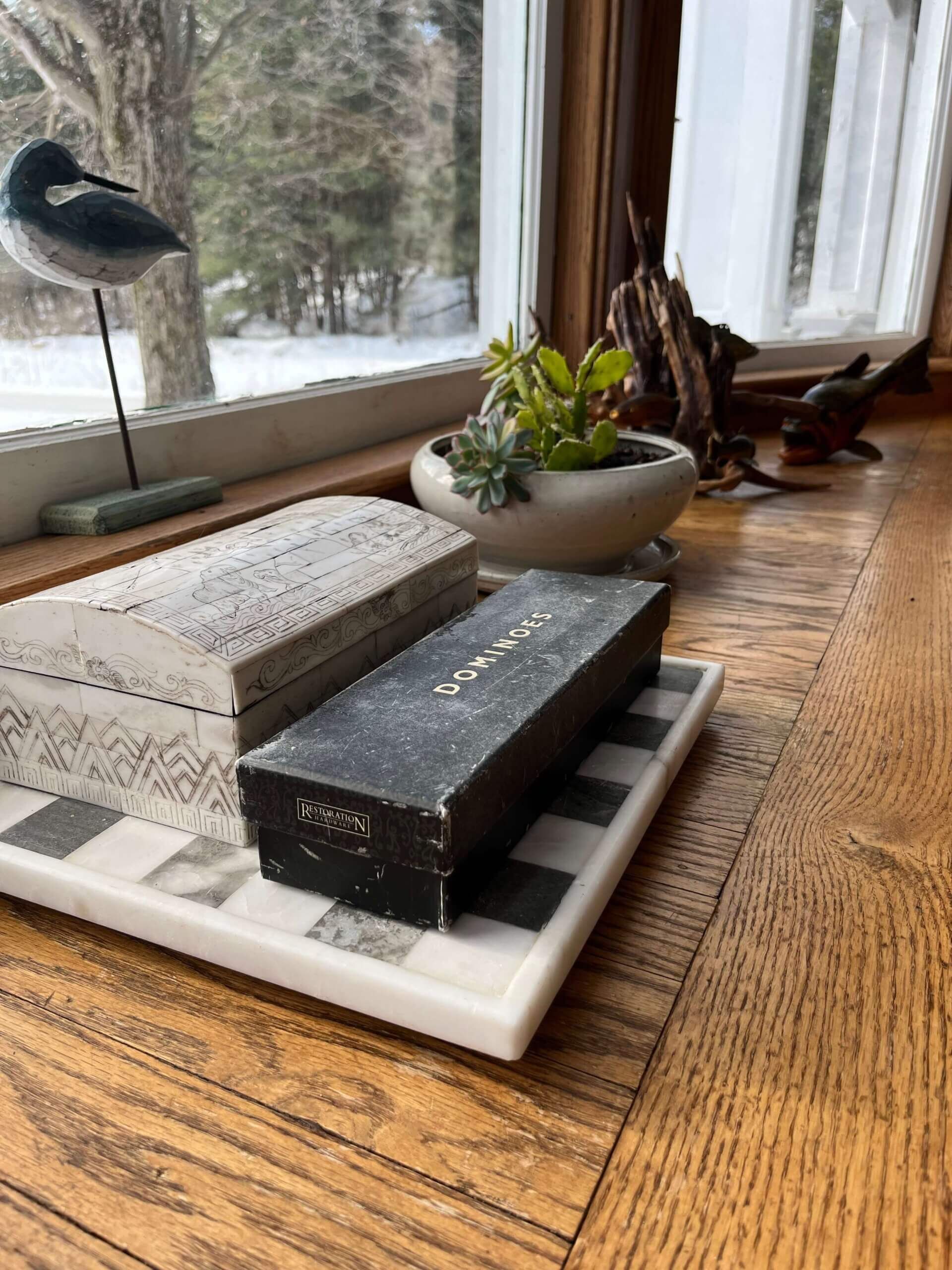 Wooden windowsill with boxes, a small plant, and a bird figurine. A snowy outdoor scene is visible.