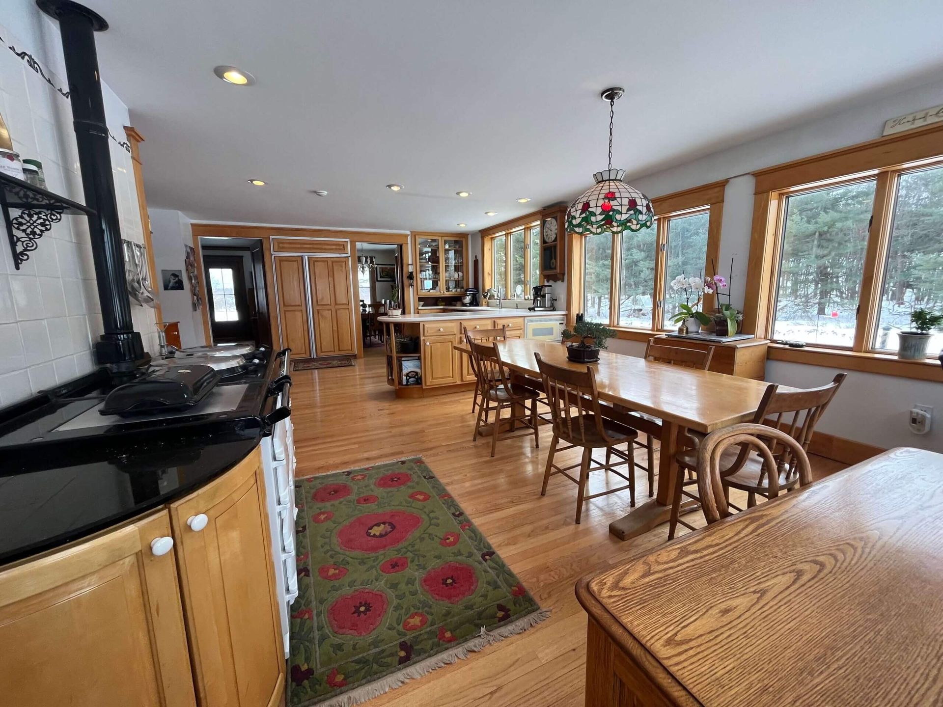 Spacious kitchen with wood cabinets, stove, and dining table near large windows overlooking a snowy landscape.