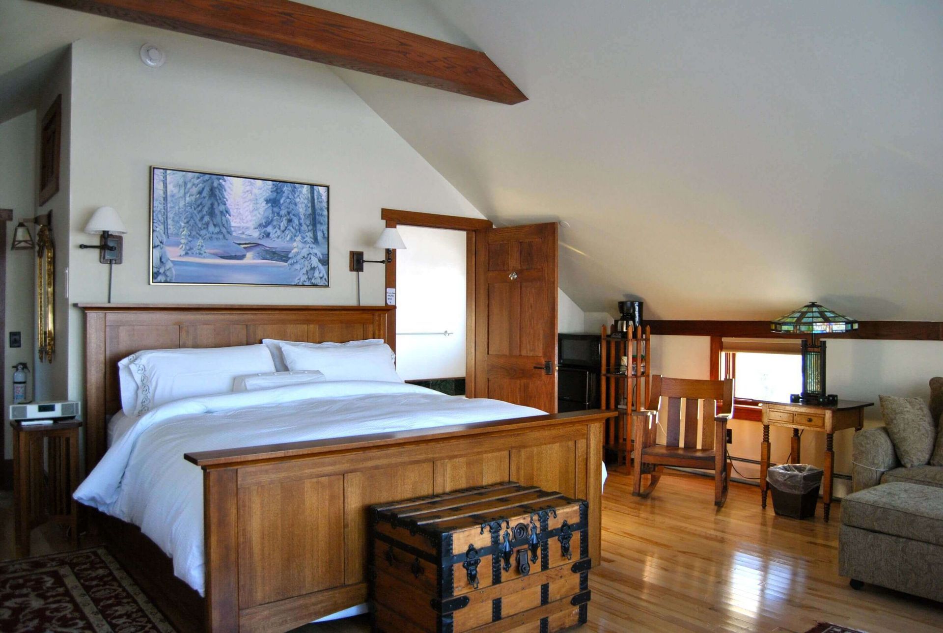 Bedroom with hardwood floors, wooden bed frame, art, trunk, and slanted ceiling.