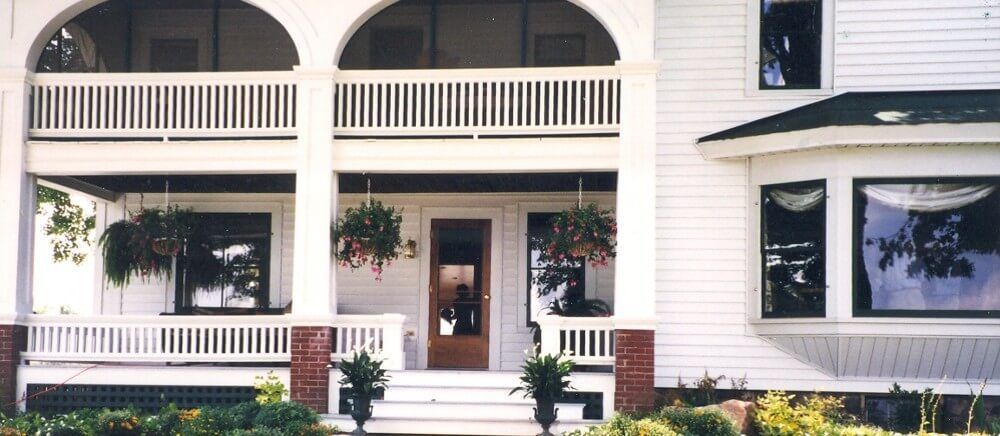 White Victorian house with porch, hanging plants, and bay windows.