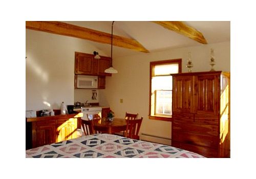 Rustic bedroom with wooden beams, bed, dresser, desk, and sunlit window