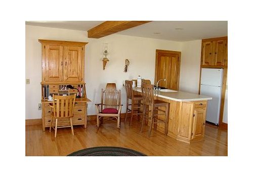 Wooden kitchen with cabinets, island, dining table, and hardwood floors in a bright room