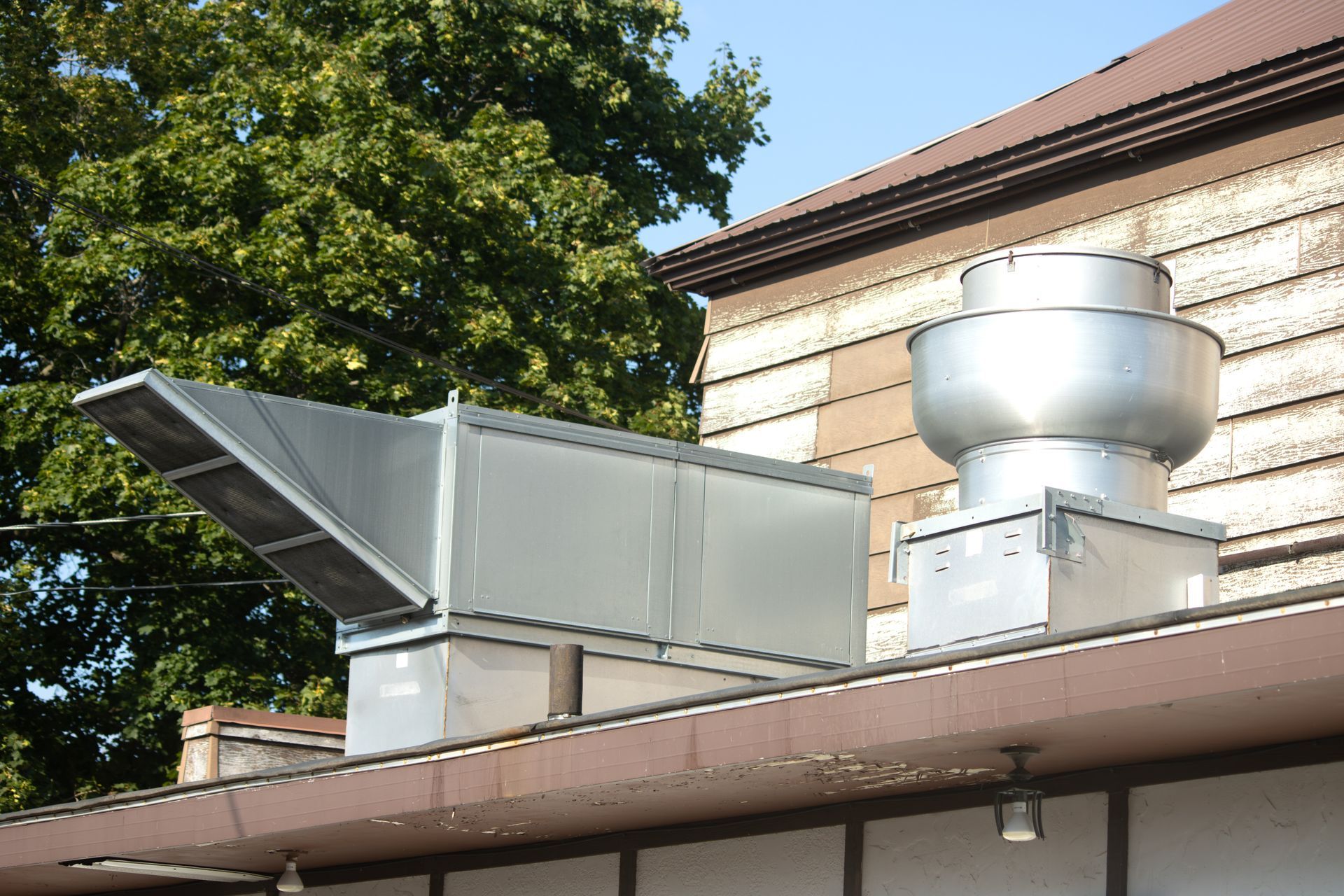 A metal exhaust system sits on a building roof, with a boxy duct and rounded vent.