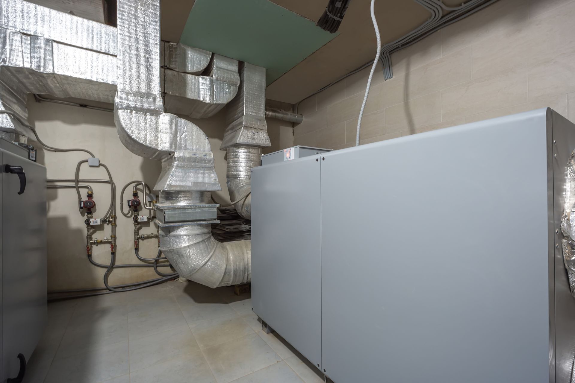 HVAC system with silver ducts and a large grey unit in a utility room.