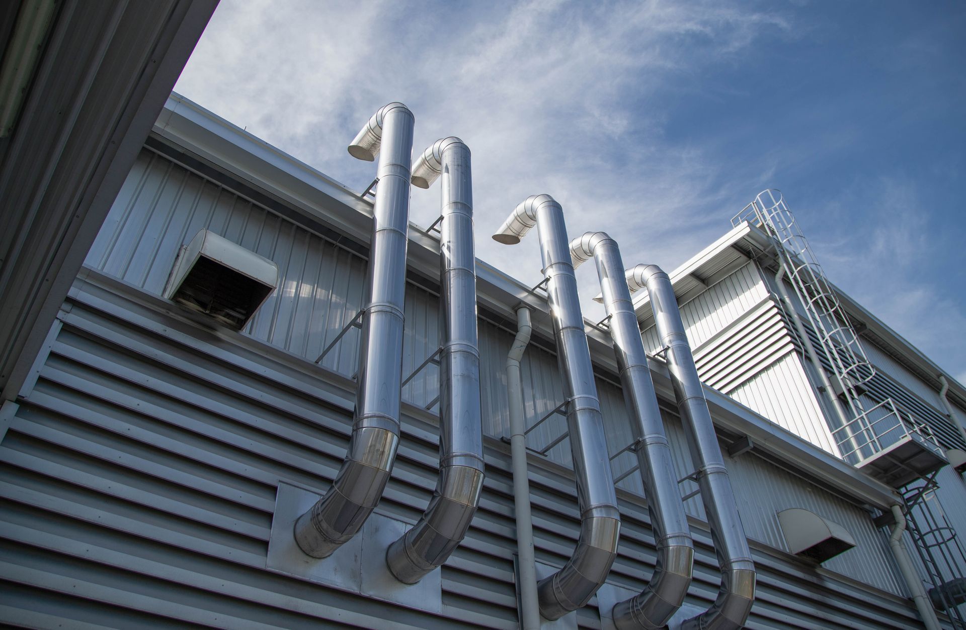 Silver pipes extending from the side of a building against a blue sky.