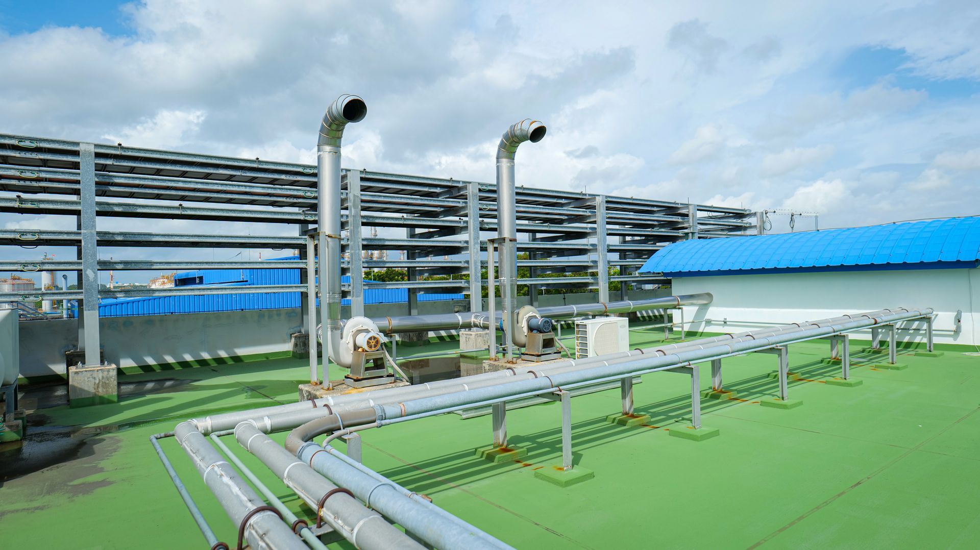 Rooftop with pipes, ventilation stacks, and support structures under a cloudy sky.