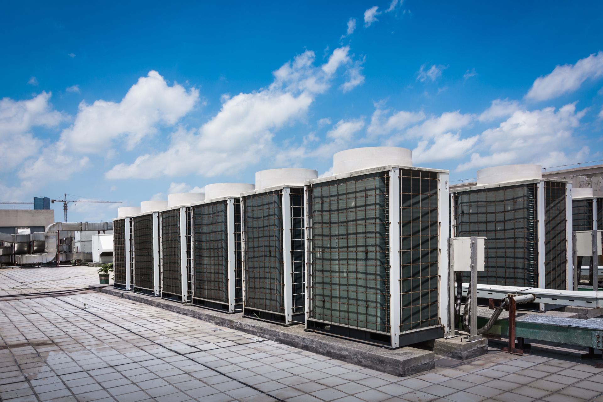 A row of industrial HVAC units on a rooftop under a blue sky with scattered clouds.
