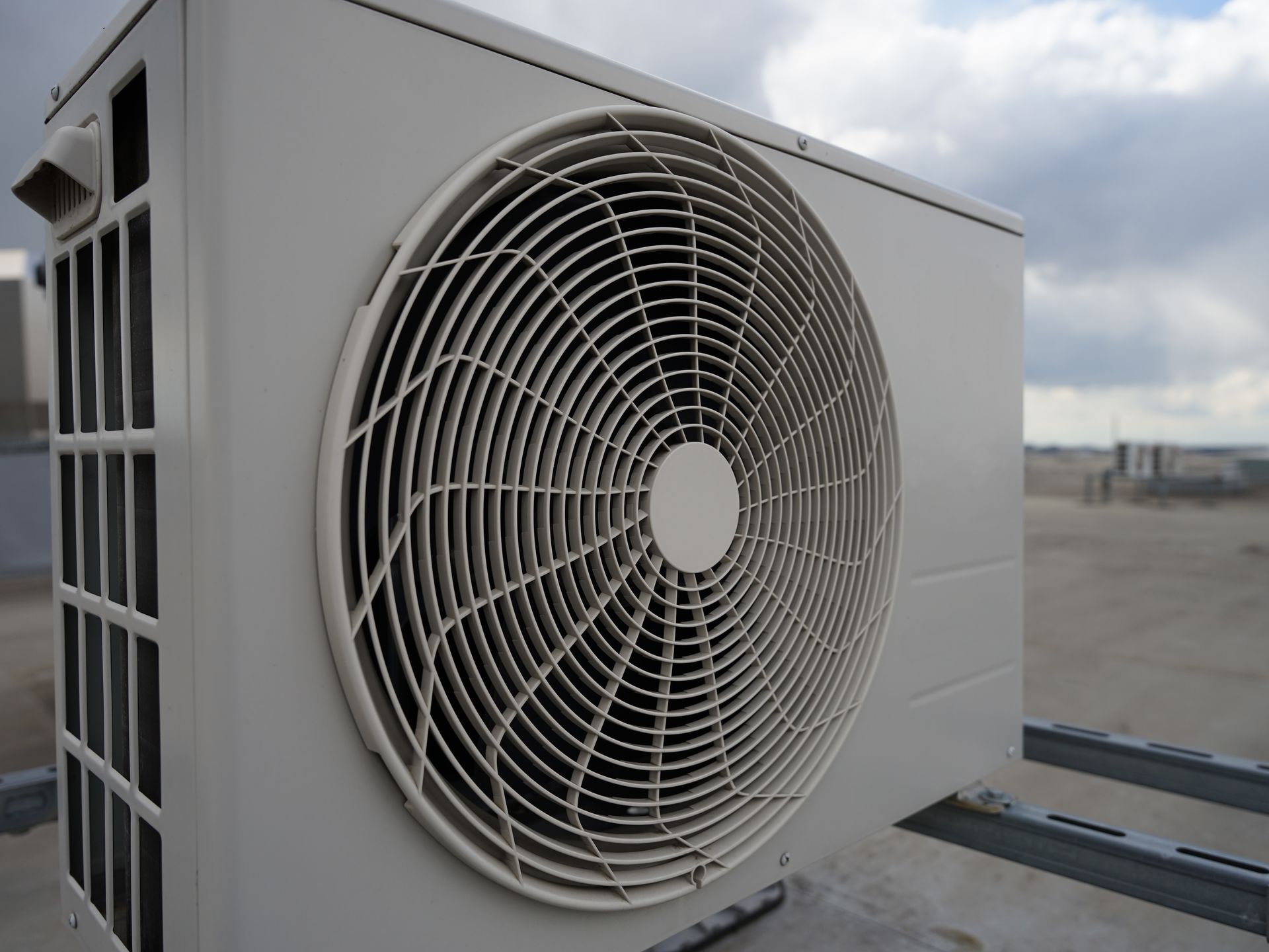 Beige outdoor air conditioning unit mounted on a metal frame against a cloudy sky.