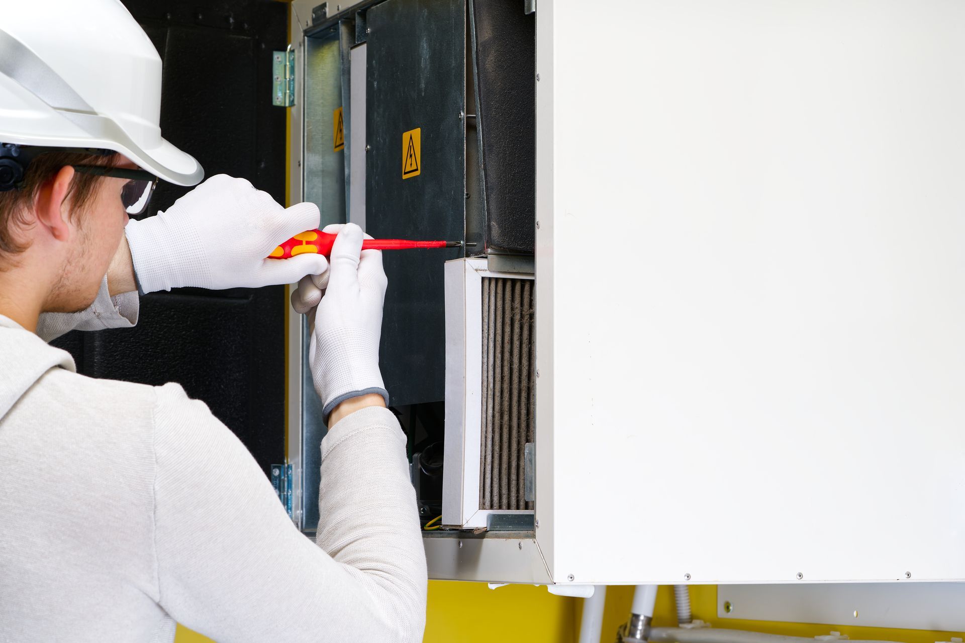 Technician in white hardhat and gloves using a screwdriver on machinery.
