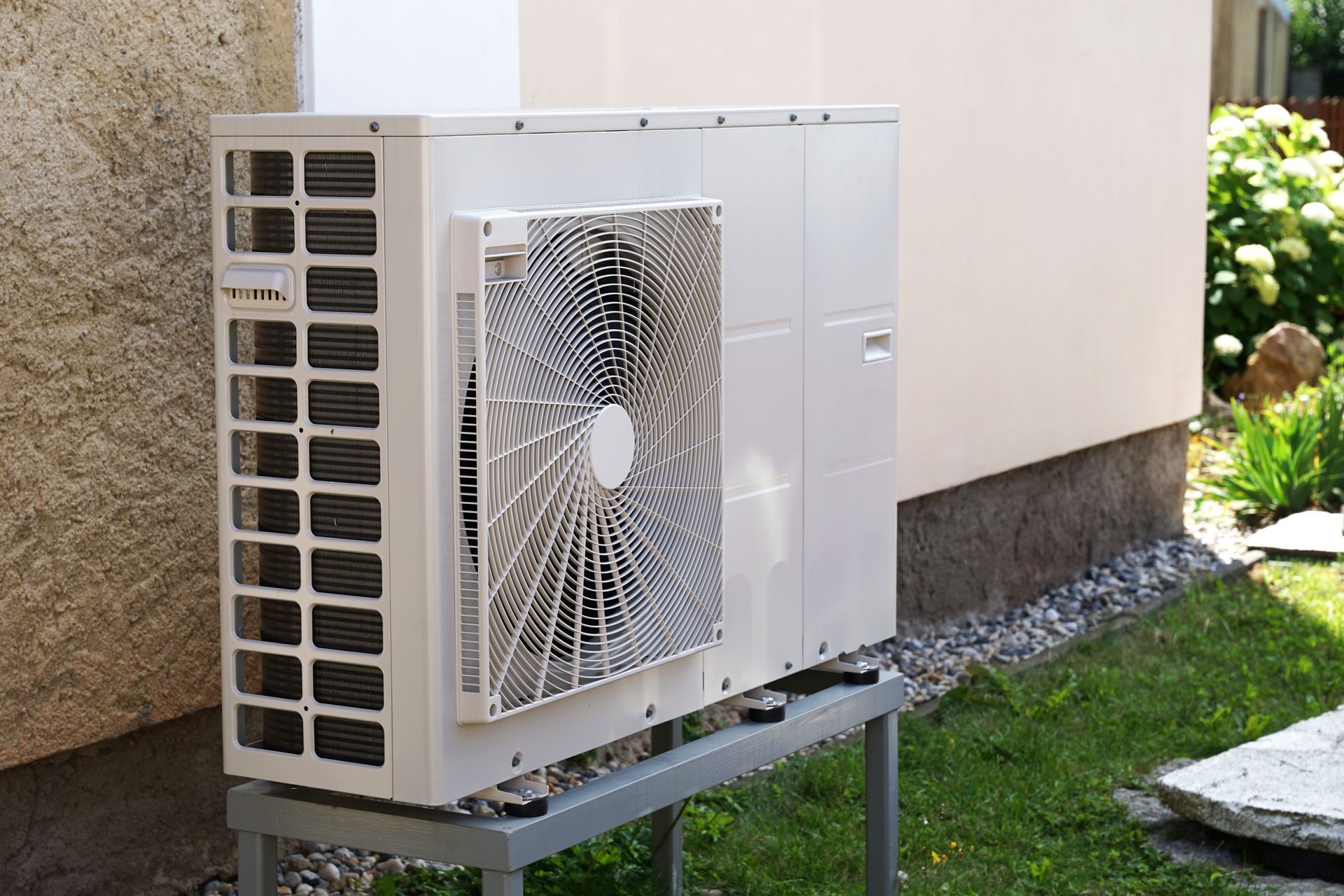 An air source heat pump unit installed outdoors on a metal stand against a building wall.