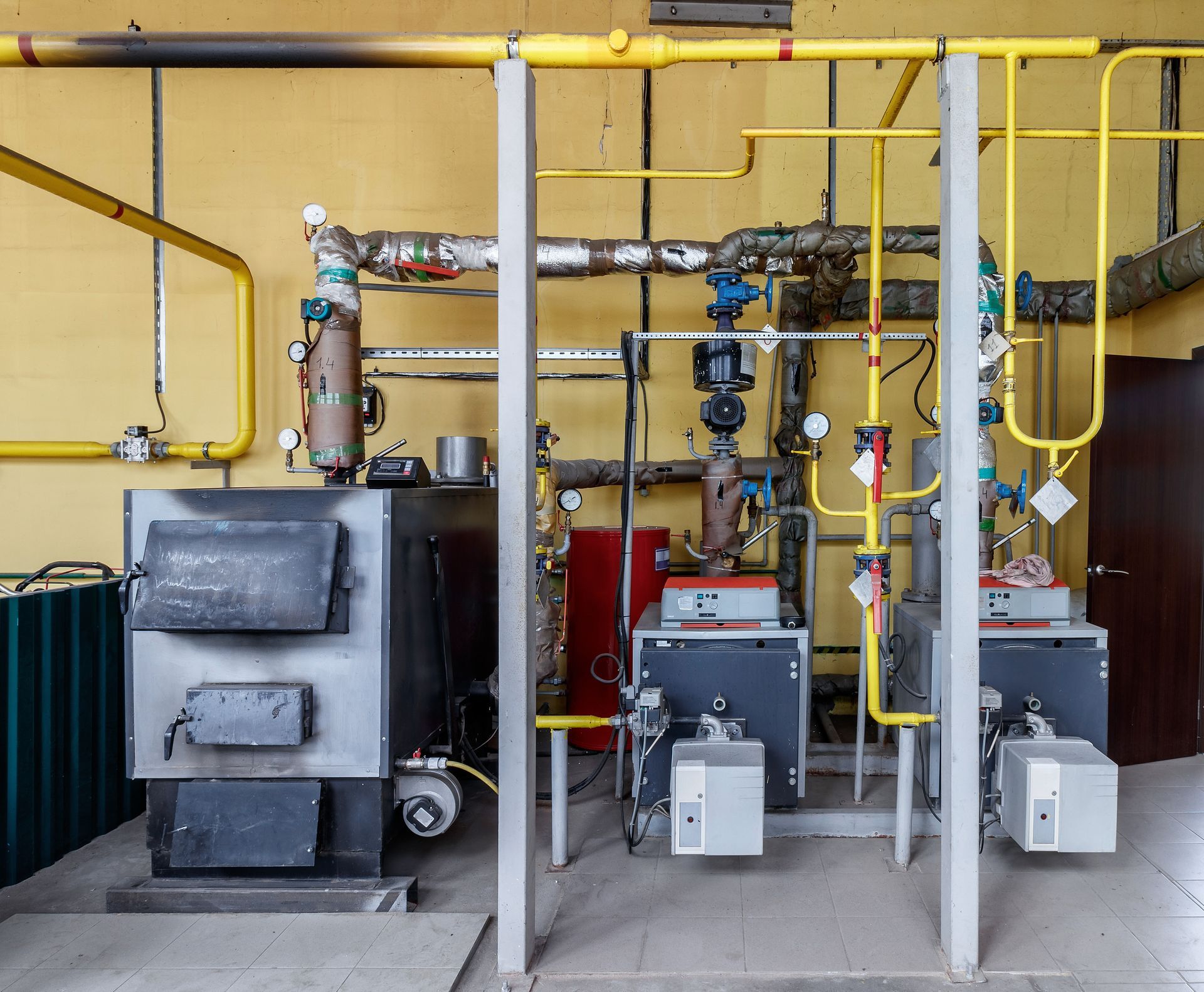 Industrial boiler room with metal machinery, yellow pipes, and a gray door.