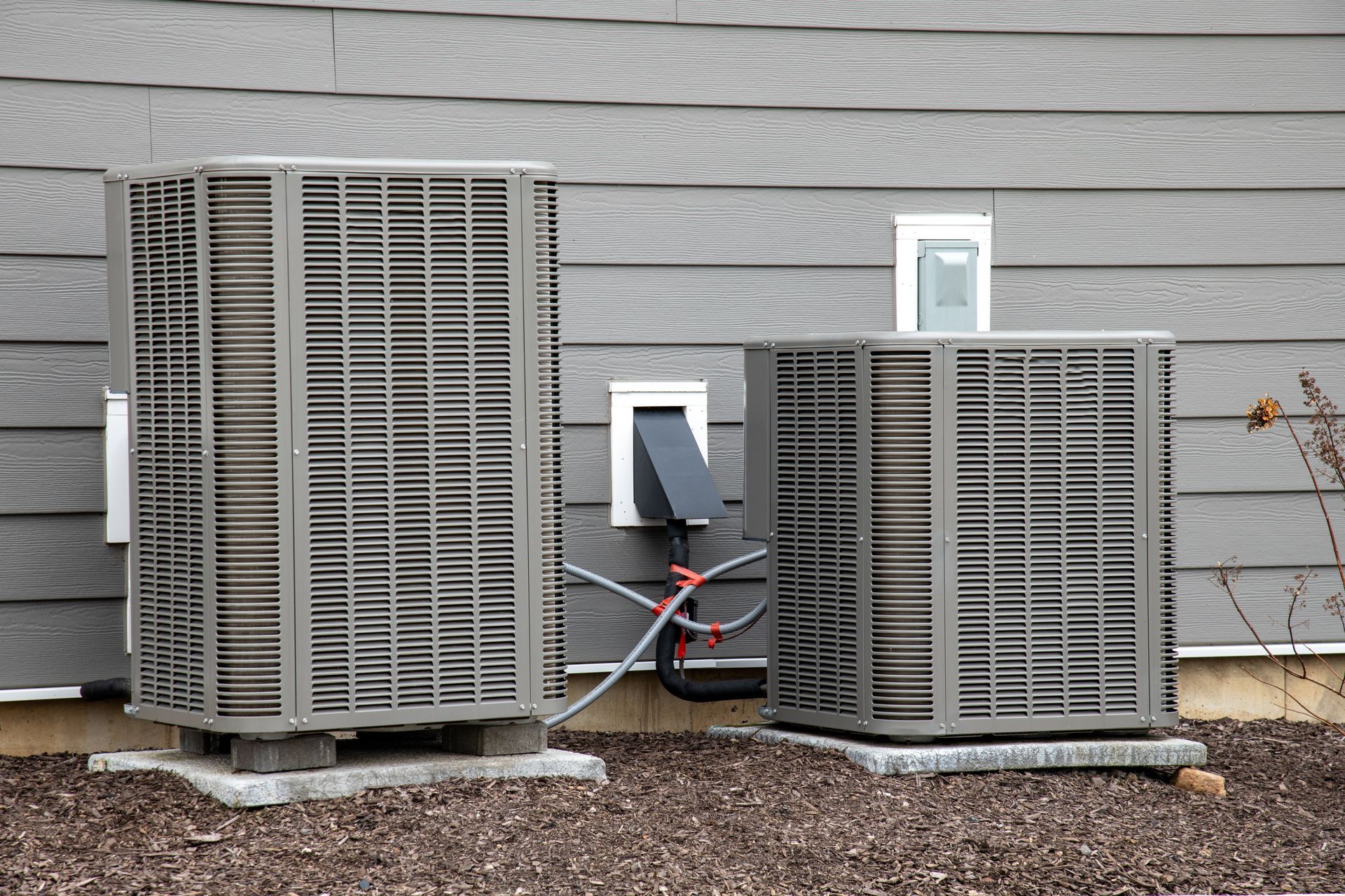 Two outdoor air conditioning units next to a gray house.