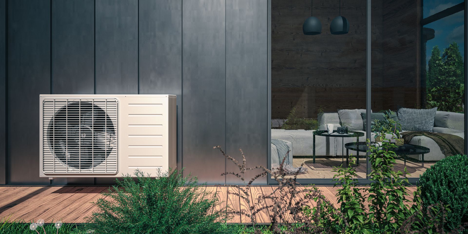 An outdoor heat pump unit sits on a wooden deck next to a modern home with glass doors and an interior lounge area.