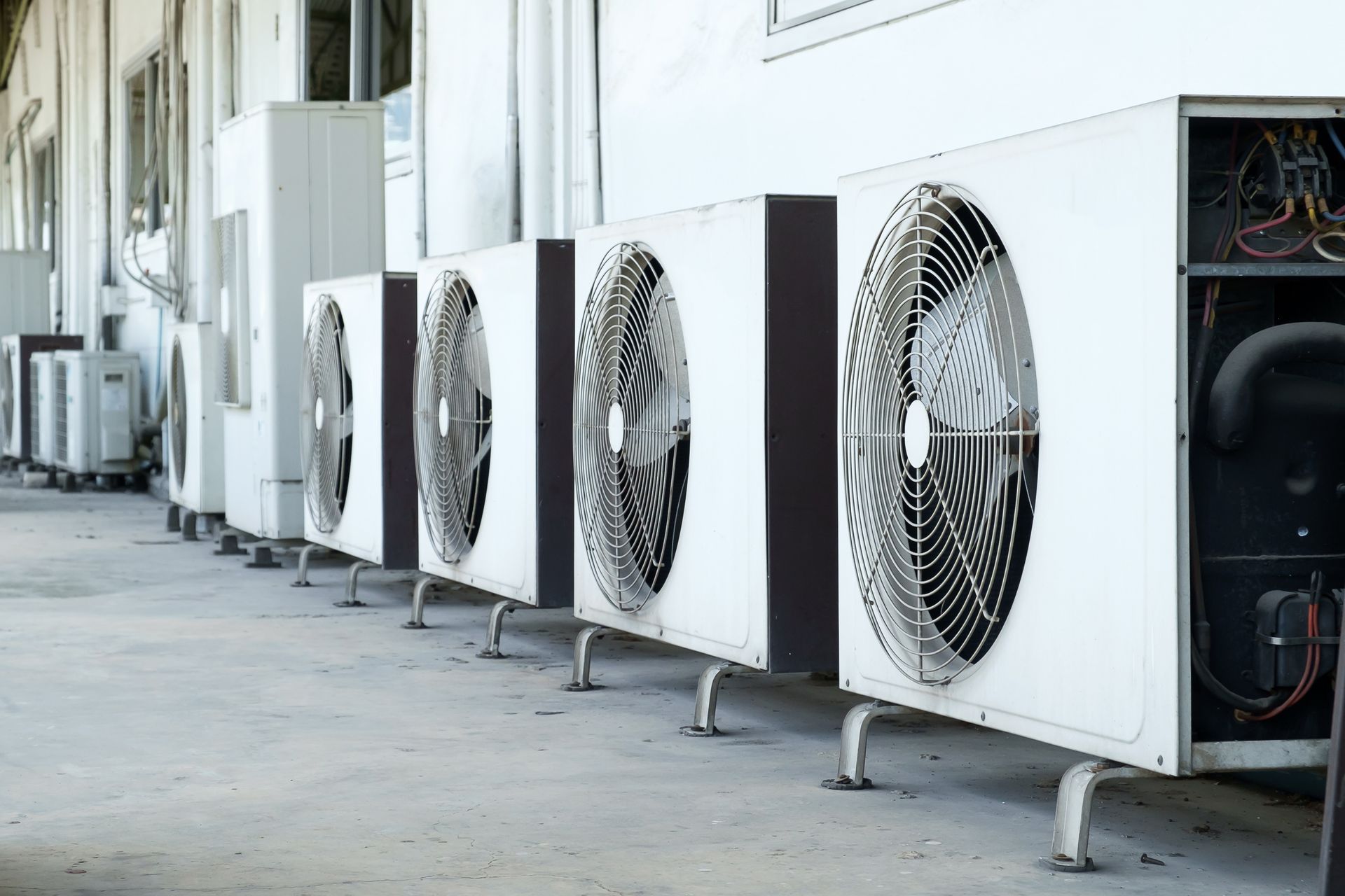 Row of white air conditioning units outside a building, with visible fans and piping.