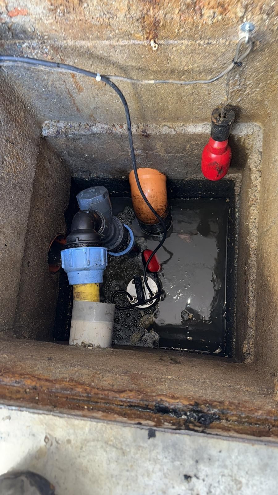 Fossa di cemento aperta con acqua e pompa; dotata di tubi, galleggiante e componenti elettrici.