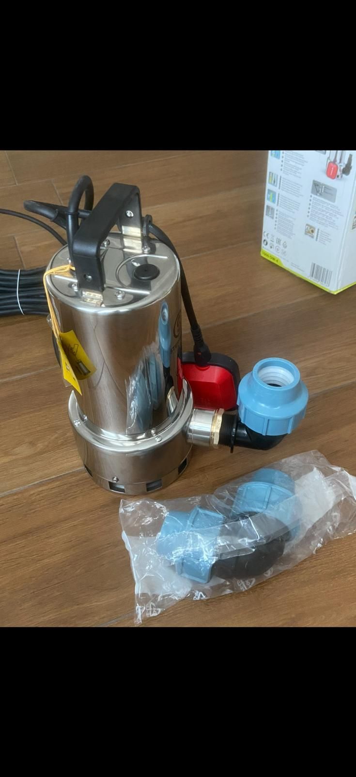 Una pompa sommersa in acciaio inossidabile con raccordi in plastica blu e una maniglia nera su una superficie di legno.
