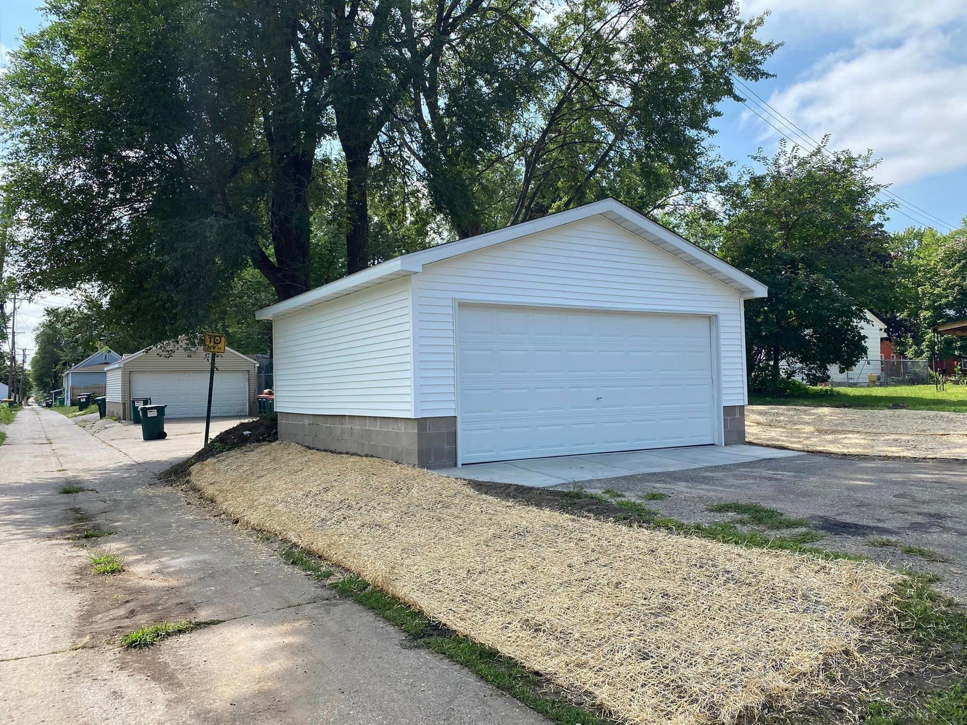 A white garage is sitting on the side of the road next to a tree.