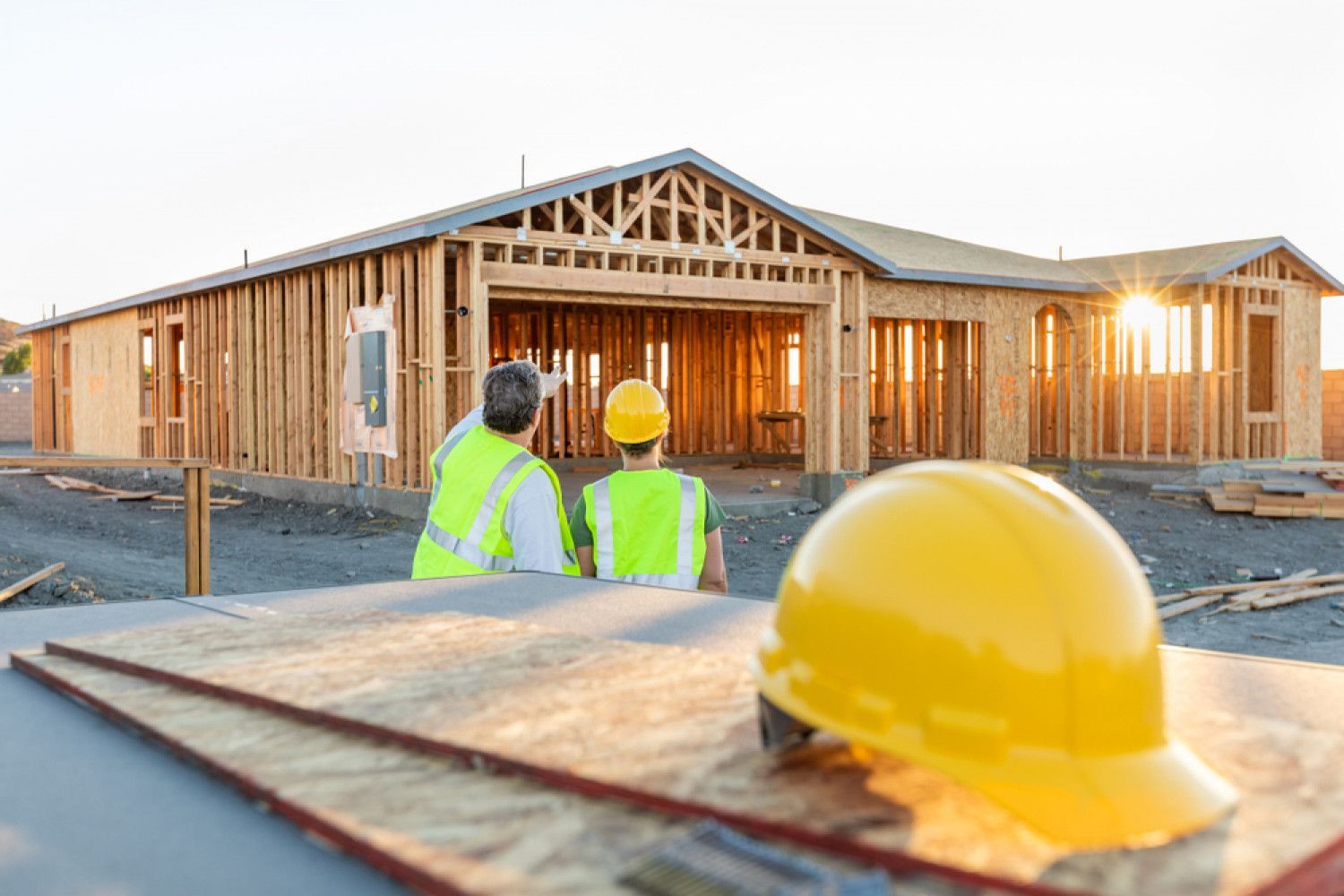 Two construction workers are looking at a house under construction.