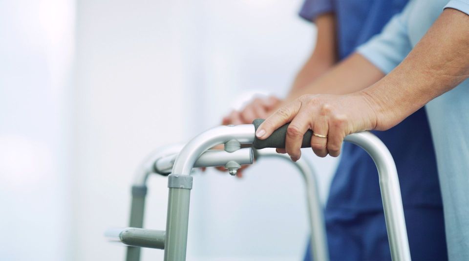 Persona che utilizza un deambulatore con l'assistenza di un operatore sanitario; ambiente interno.