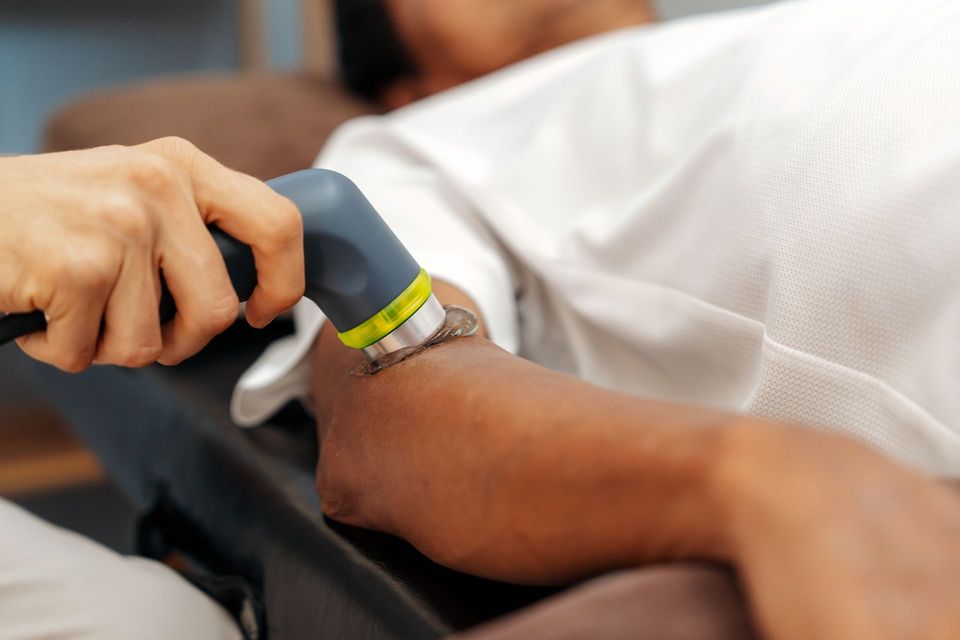 Il terapista utilizza un dispositivo sul braccio del paziente per la terapia a ultrasuoni. Mano dalla pelle chiara, toni neutri, in interni.