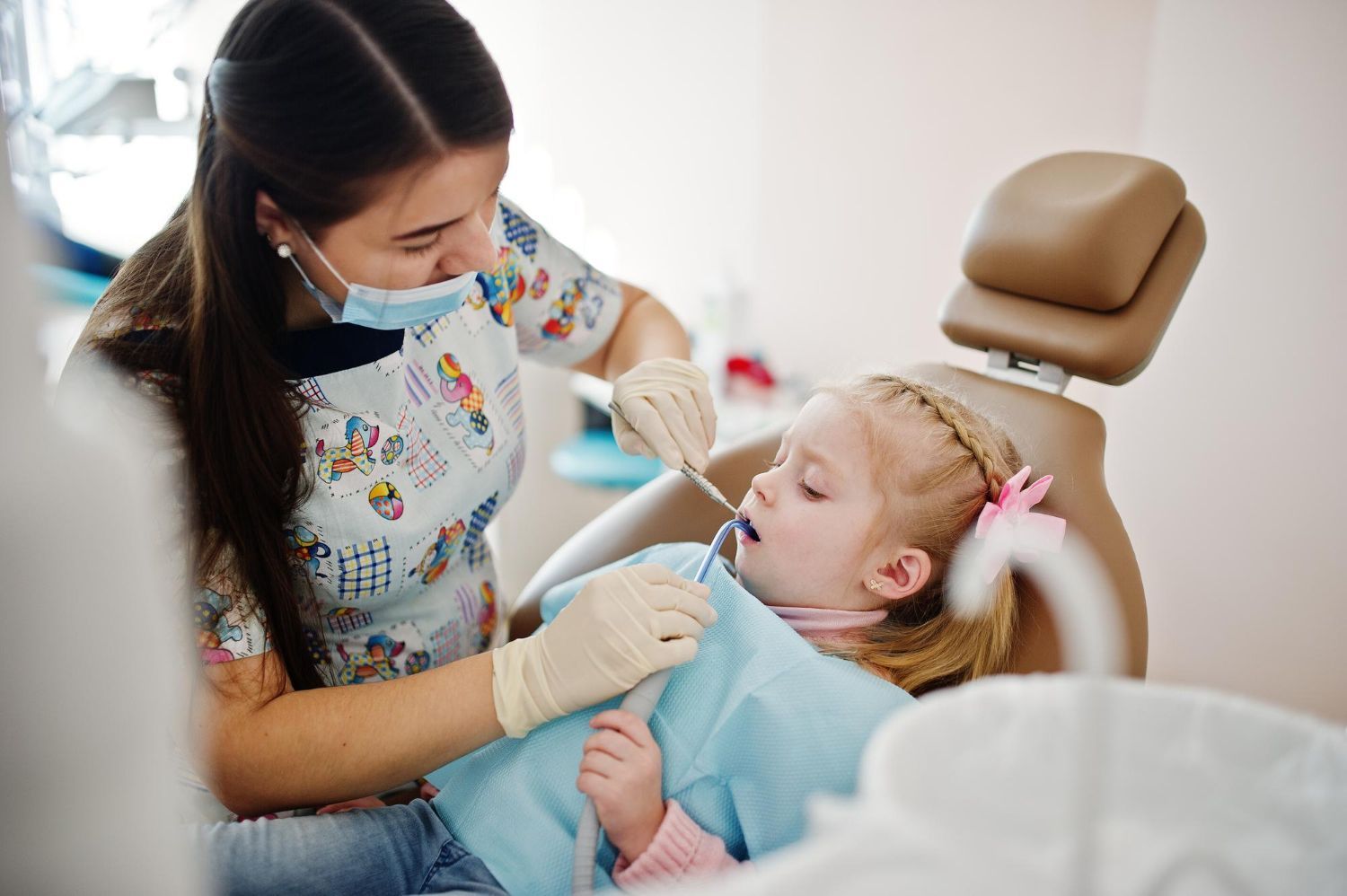 A little girl is sitting in a dental chair while a dentist examines her teeth.