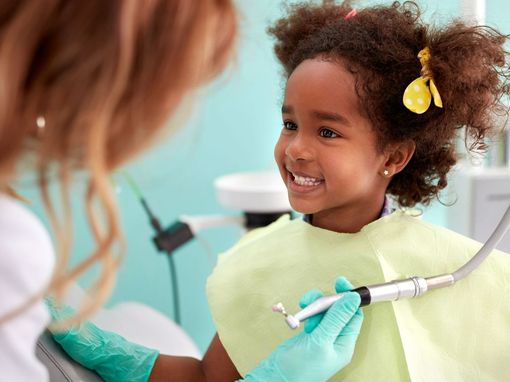 A little girl is sitting in a dental chair getting her teeth examined by a dentist.