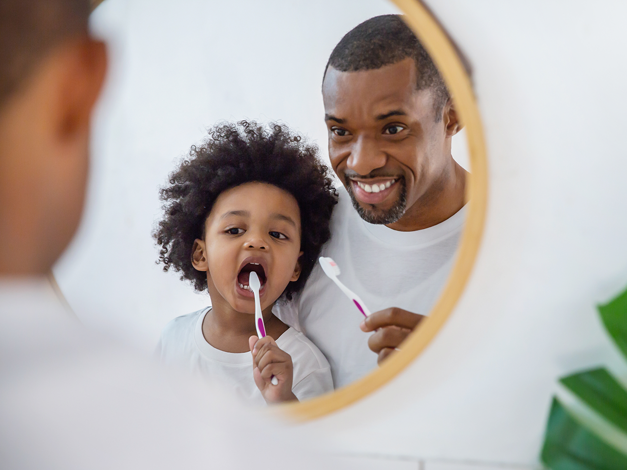 A man and a child are brushing their teeth in front of a mirror.