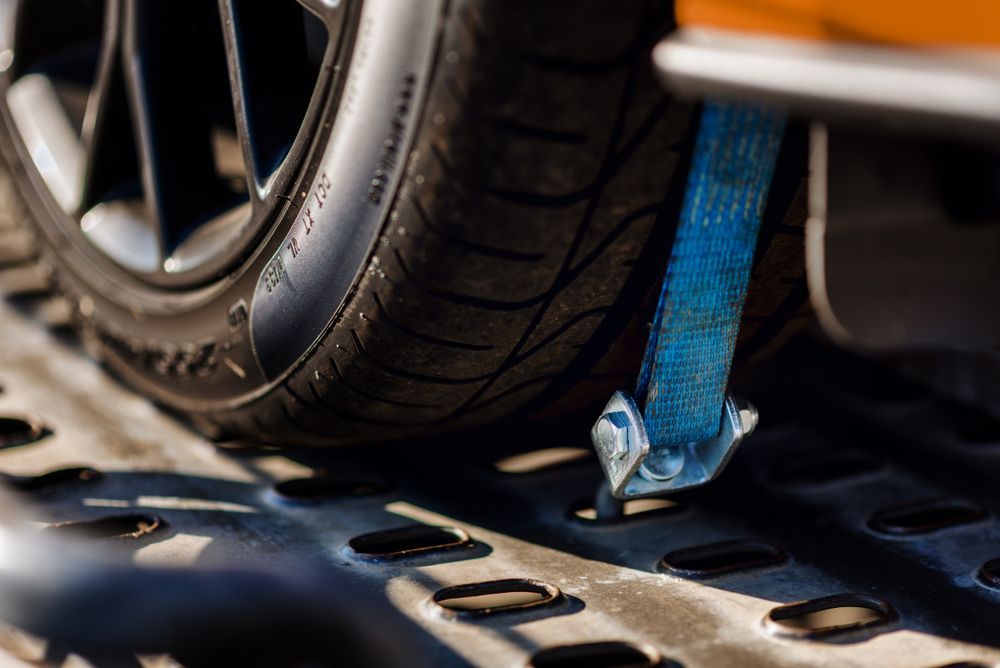 Close-up of a Car Tire Secured to a Flatbed Tow Truck With a Blue Strap — Old Mate's Towing Townsville in Deeragun, QLD