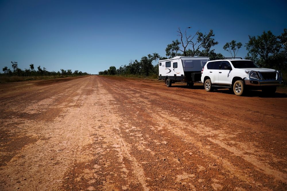 White Suv Towing a Silver Camper Trailer on a Red Dirt Road — Old Mate's Towing Townsville in Deeragun, QLD