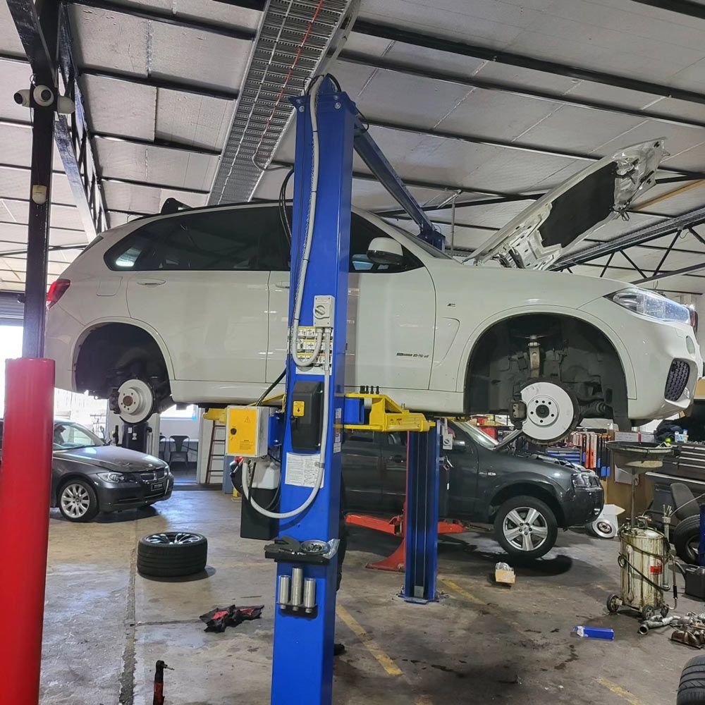 A White Car Is Sitting on Top of A Blue Lift in A Garage — Powatone Exhaust Centre in Fyshwick, ACT