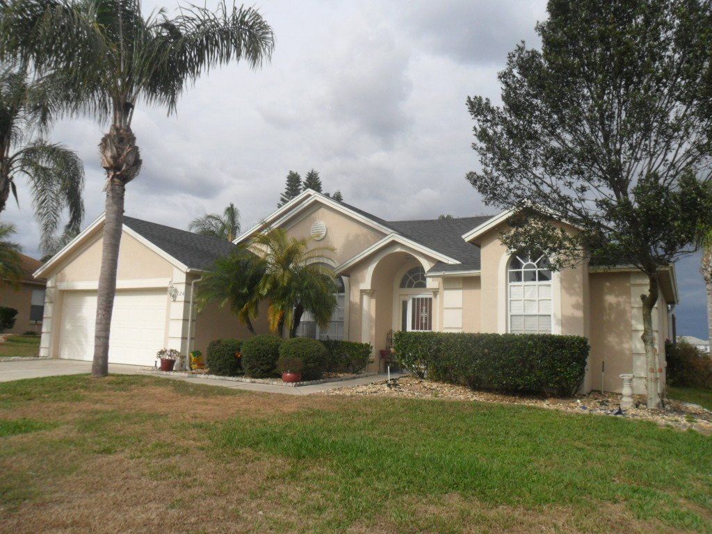 Cream colored house with gray roof and two trees out front.