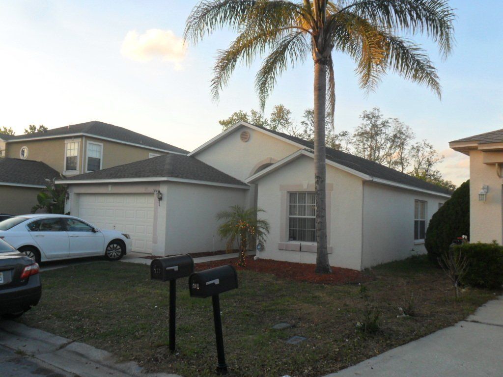White house with a gray roof, a white car out front and one tree.
