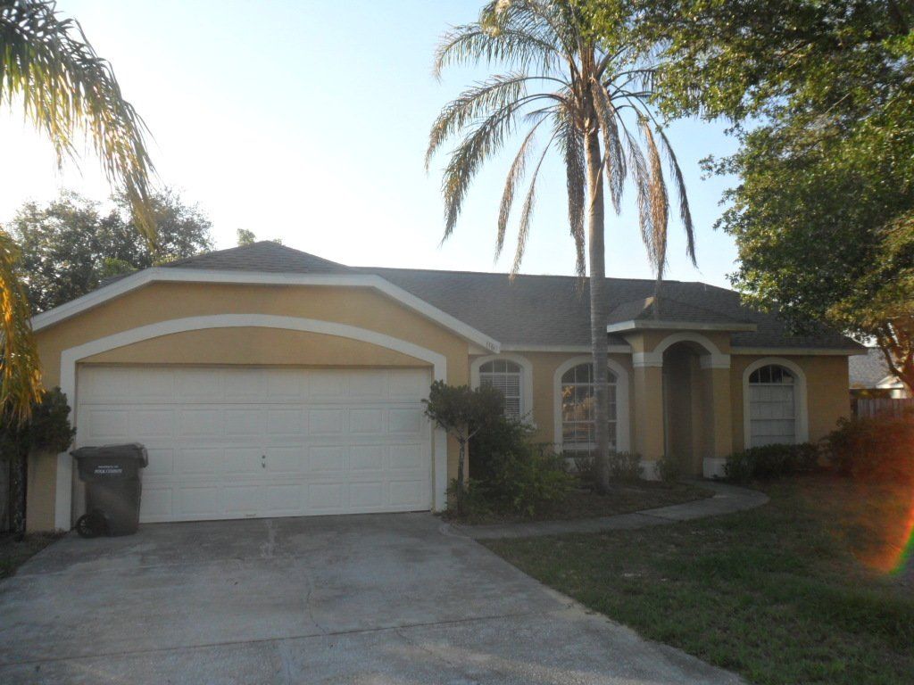 Tan and yellow house with a gray roof, garbage can and tree in front of it.