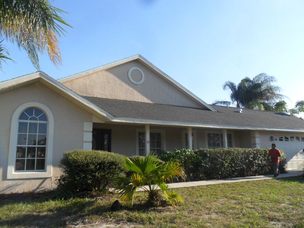 Tan house with a gray roof and a line of bushes in front of it.