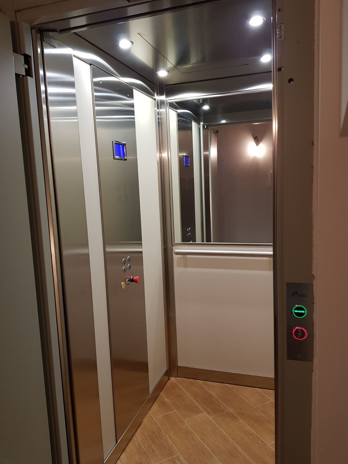 Un ascensore in acciaio inossidabile con pavimento in legno e specchio.