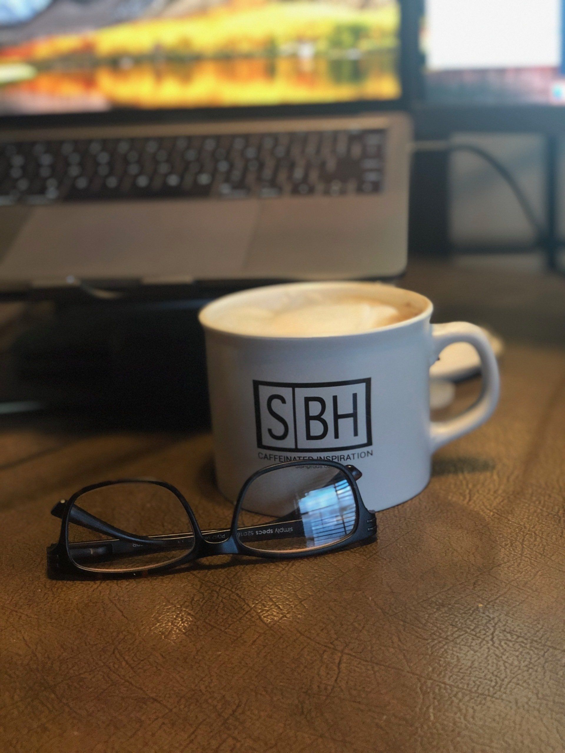 laptop plugged into dock, black glasses, coffee mug (studiobeanhead swag)
