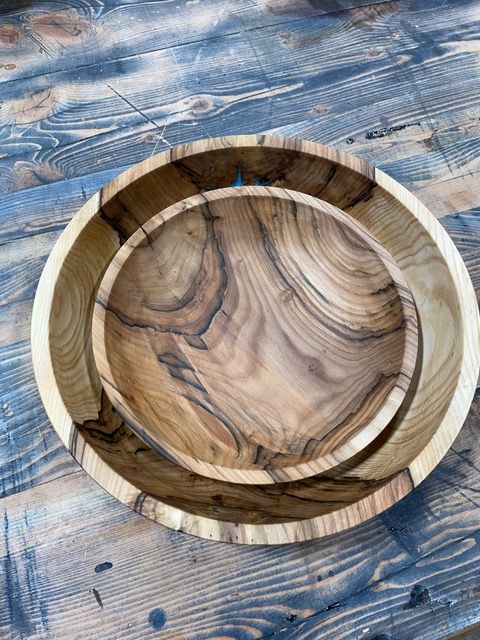 Two wooden bowls, nested inside each other, with visible wood grain on a rustic wooden surface.