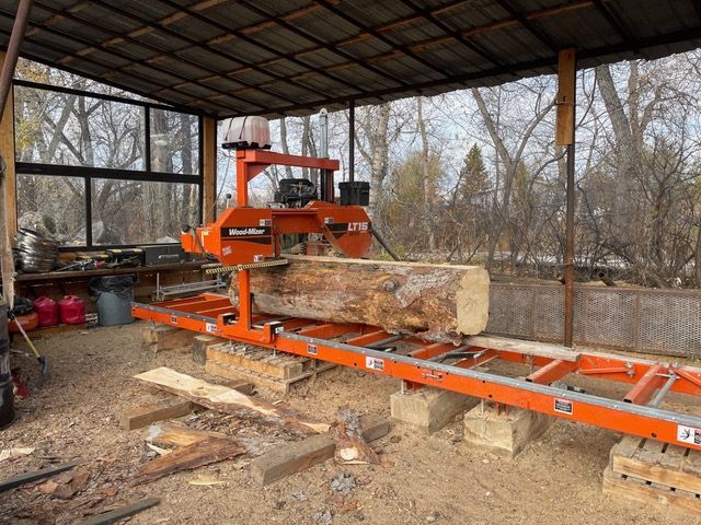 Orange sawmill cutting a large log in a covered outdoor space.