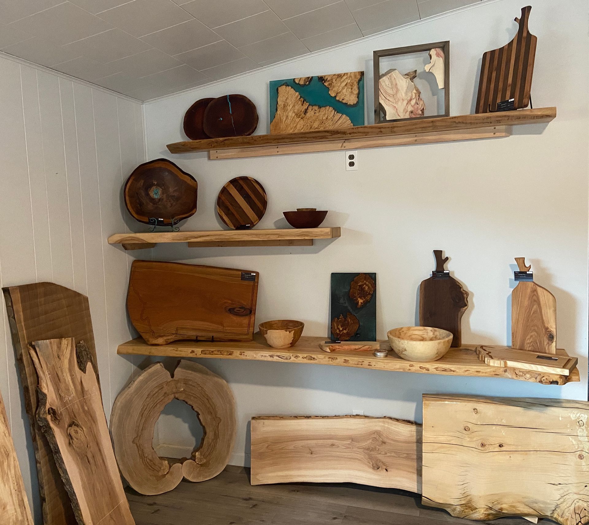 Wooden shelves displaying handcrafted cutting boards and wooden decor against a white wall.