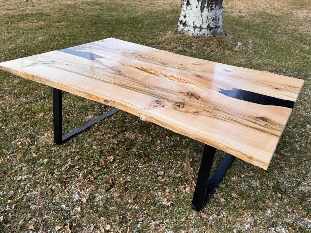Live edge wooden table with black resin, black metal legs, outdoors.