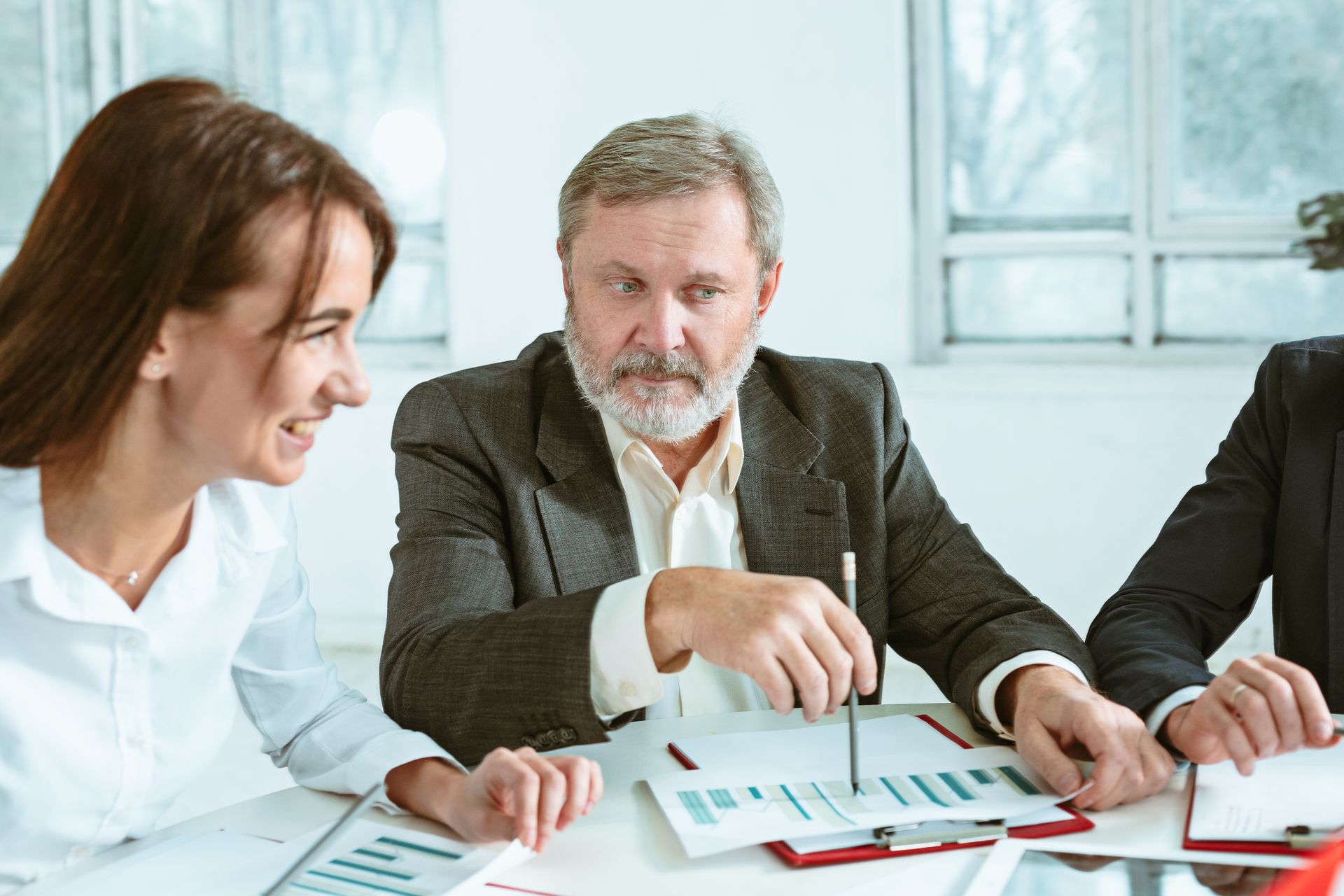 A diverse business meeting: A woman smiles, while a man in a suit gestures at charts.
